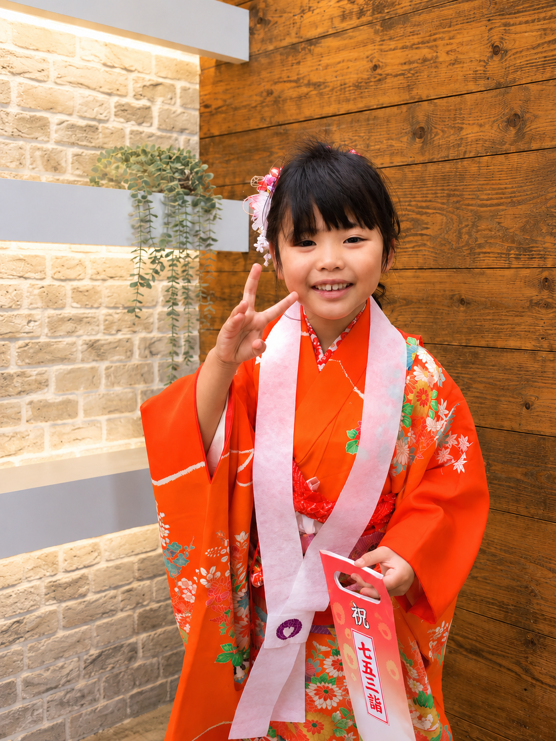 オレンジ色の着物姿で笑顔のピースサインをする七五三の女の子